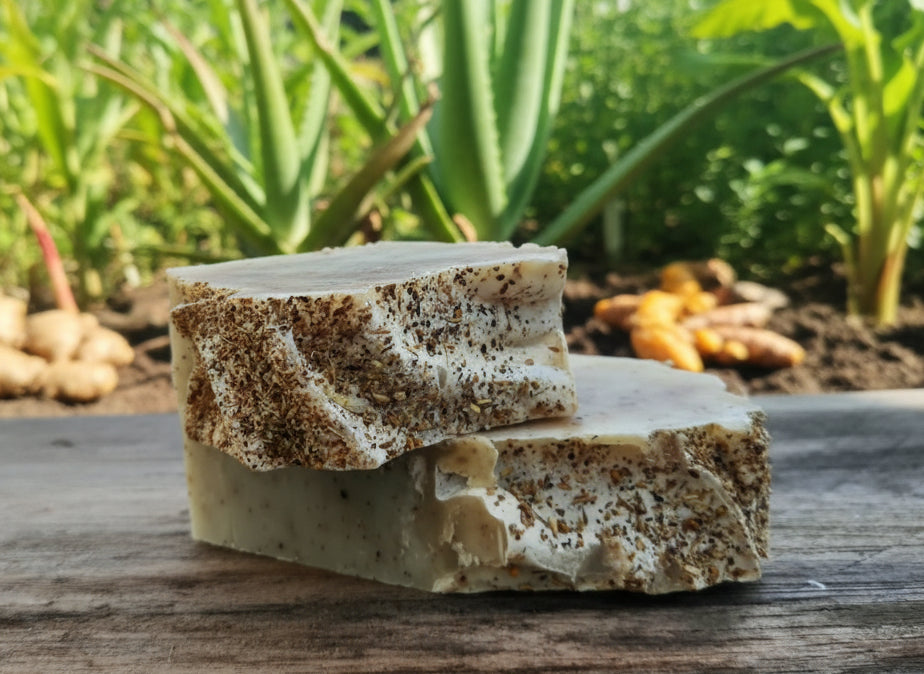 Handmade organic ginger turmeric aloe body bar with orange peel flecks and turmeric swirl, golden glow on bamboo soap dish, spa wellness vibe