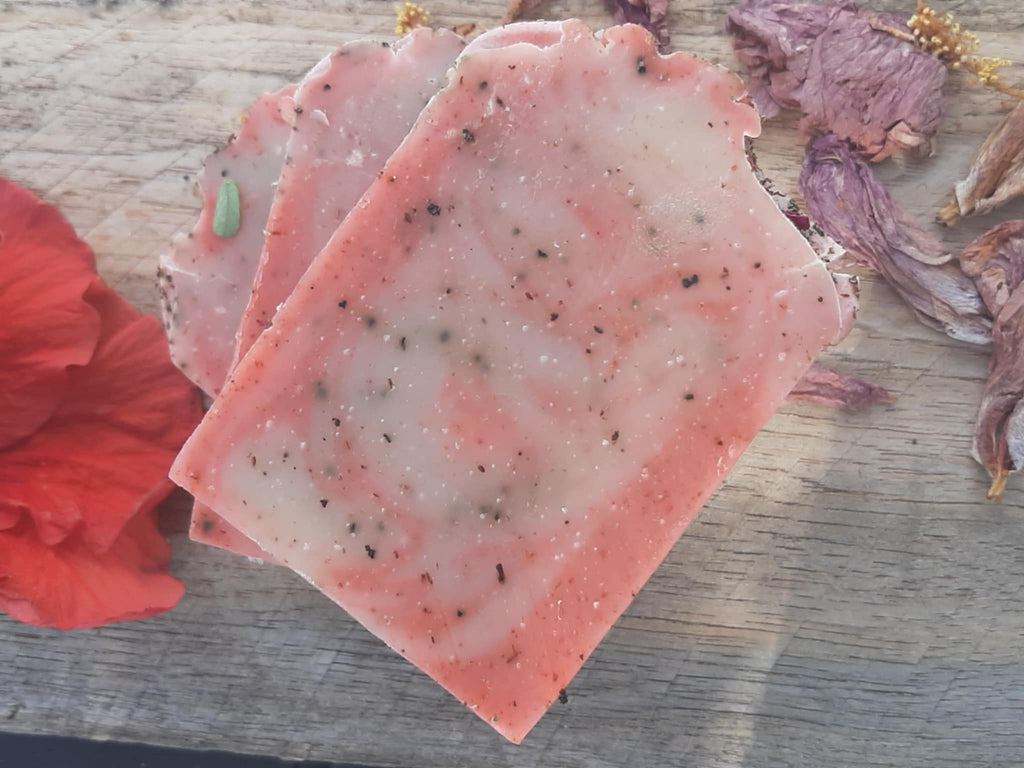 Handmade organic hibiscus tea aloe and nectar body bar with dried hibiscus petals and aloe flecks, vibrant pink swirl, on marble with fresh flowers