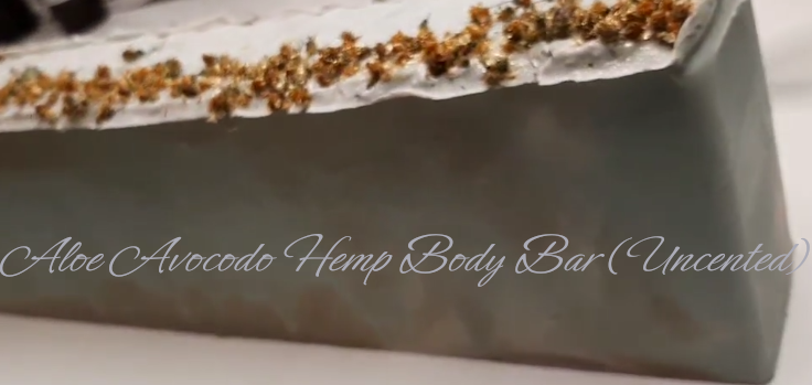 Handmade organic unscented tallow aloe avocado bentonite hemp body bar with green clay swirl and dried herbs, on white stone with fresh aloe leaf, clean spa minimalism